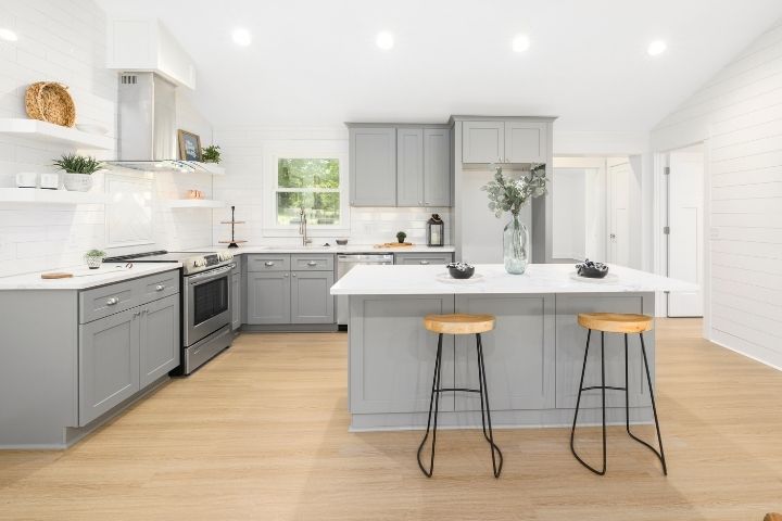 A modern kitchen featuring gray base cabinets transformed via cabinet refacing, white subway-tile walls, and a white central island with wooden stools. A modern kitchen featuring gray base cabinets transformed via cabinet refacing, white subway-tile walls, and a white central island with wooden stools.
