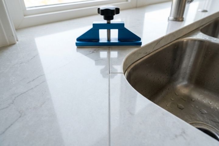 Specialized installer tools leveling a quartz seam near the sink cutout during countertop resurfacing. Specialized installer tools leveling a quartz seam near the sink cutout during countertop resurfacing.