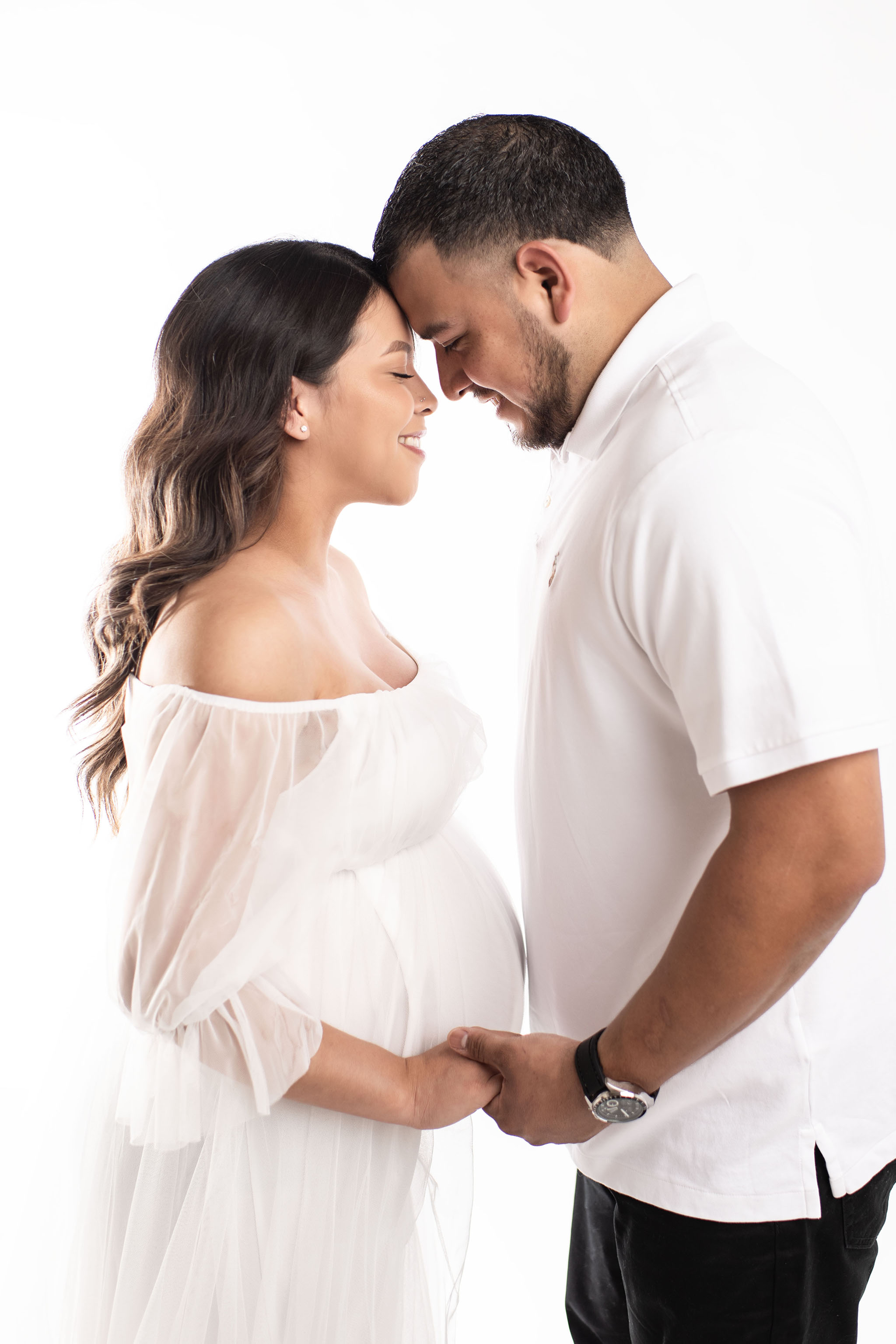 A pregnant woman in a white dress holding hands with her husband