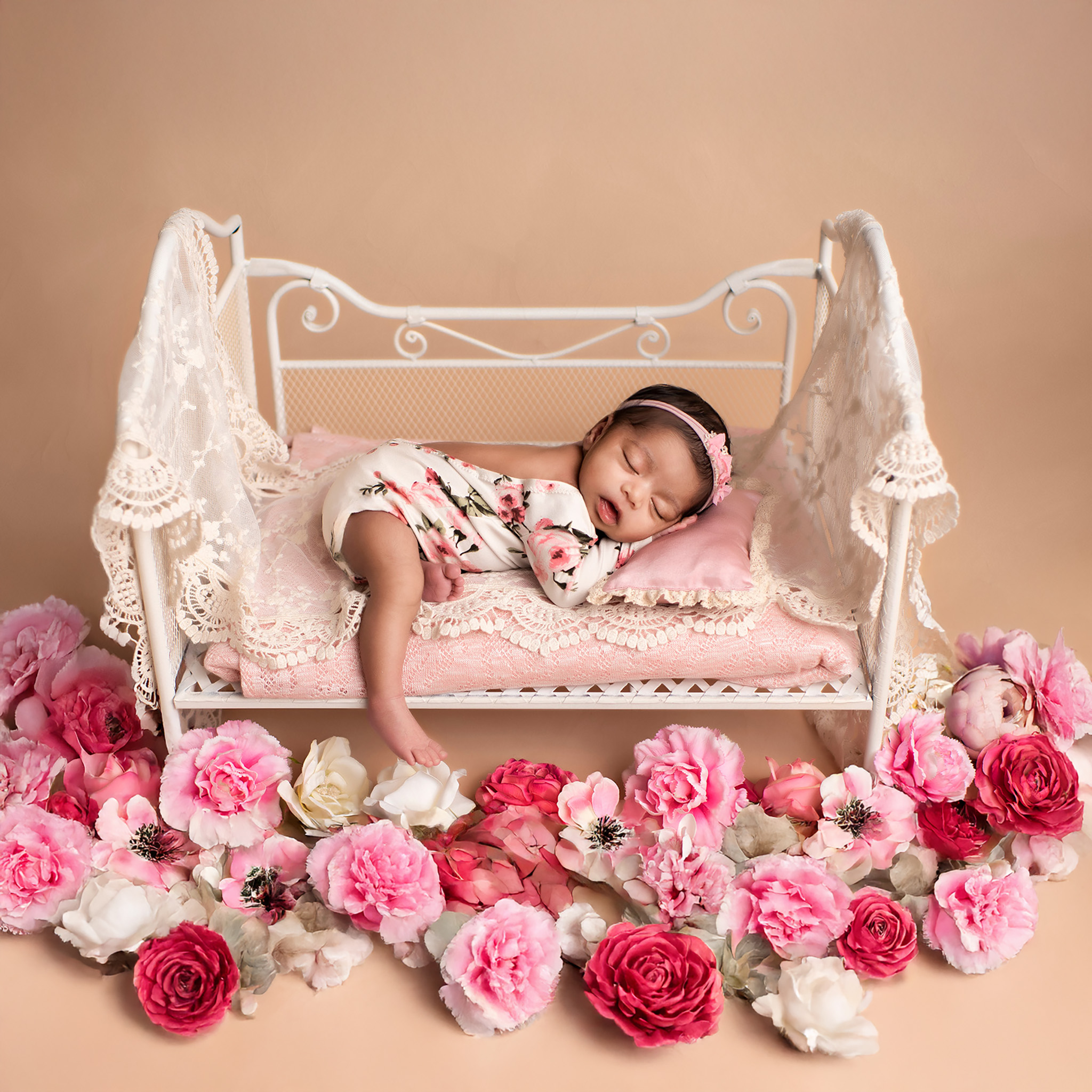 Newborn baby girl sleeping on white bed with flowers all around the bed