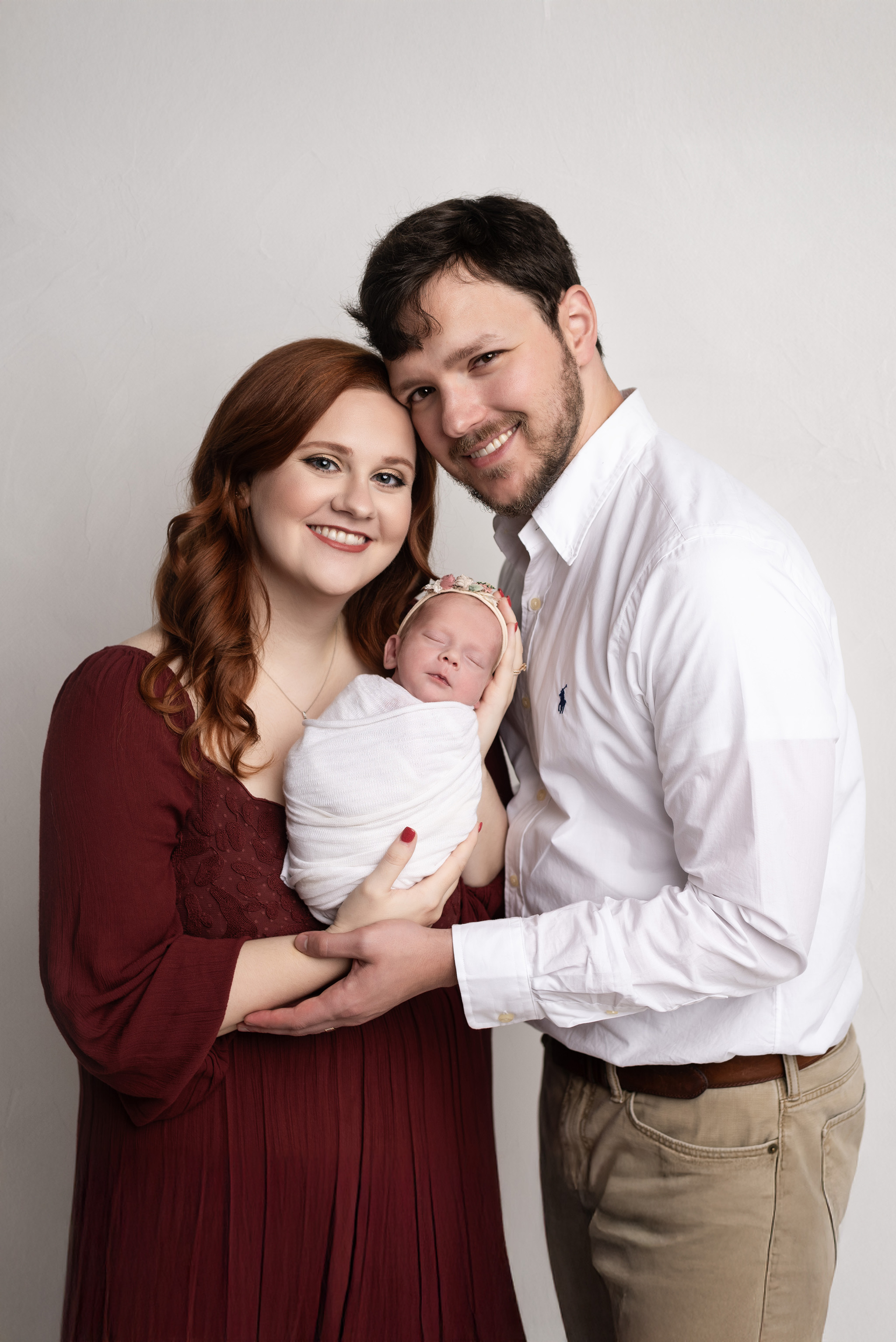 Smiling mother and father holding newborn baby girl in white swaddle.