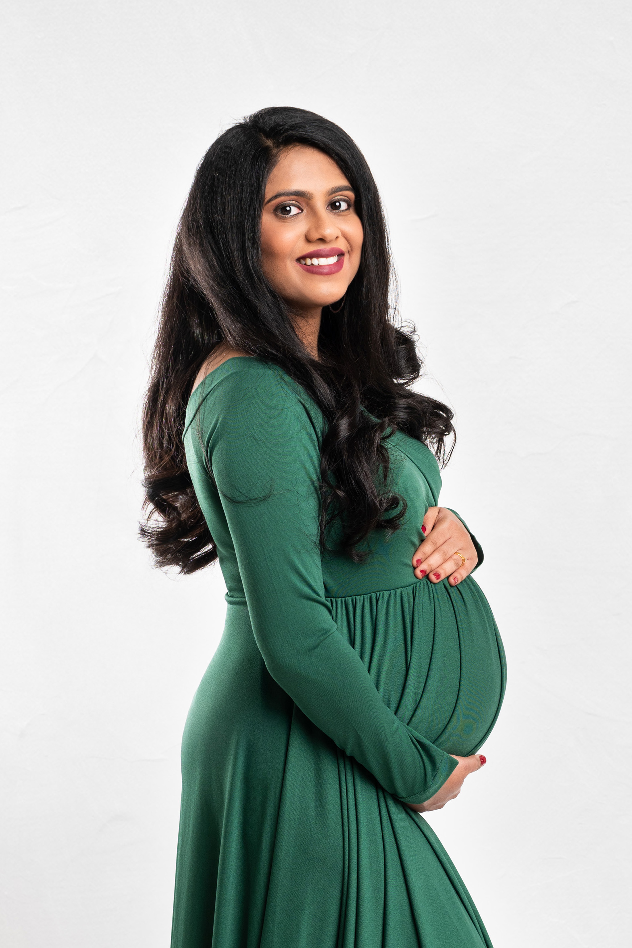 Pregnant Indian woman in green dress smiling at camera.