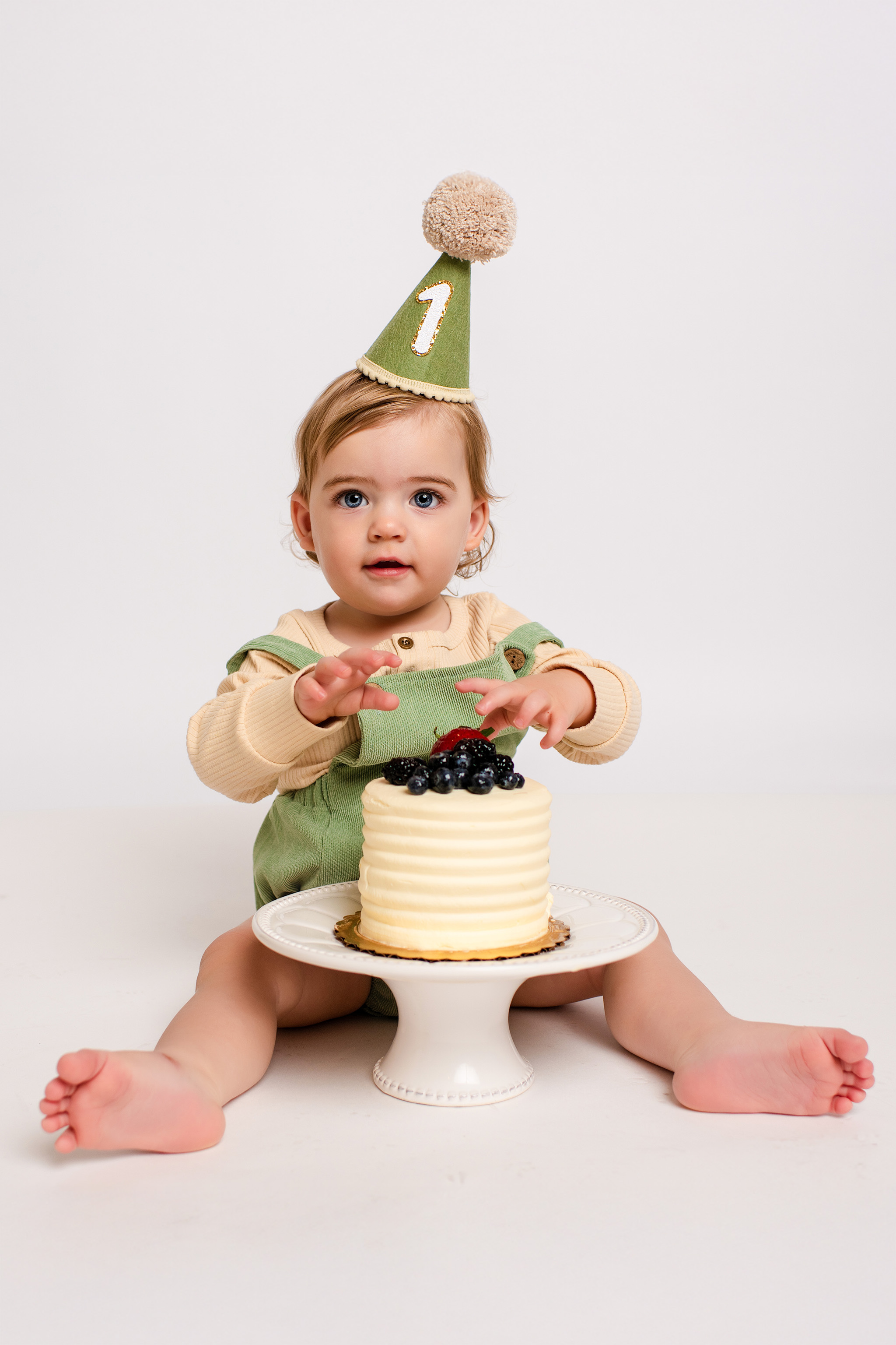 1st birthday boy with white cake and green birthday hat.