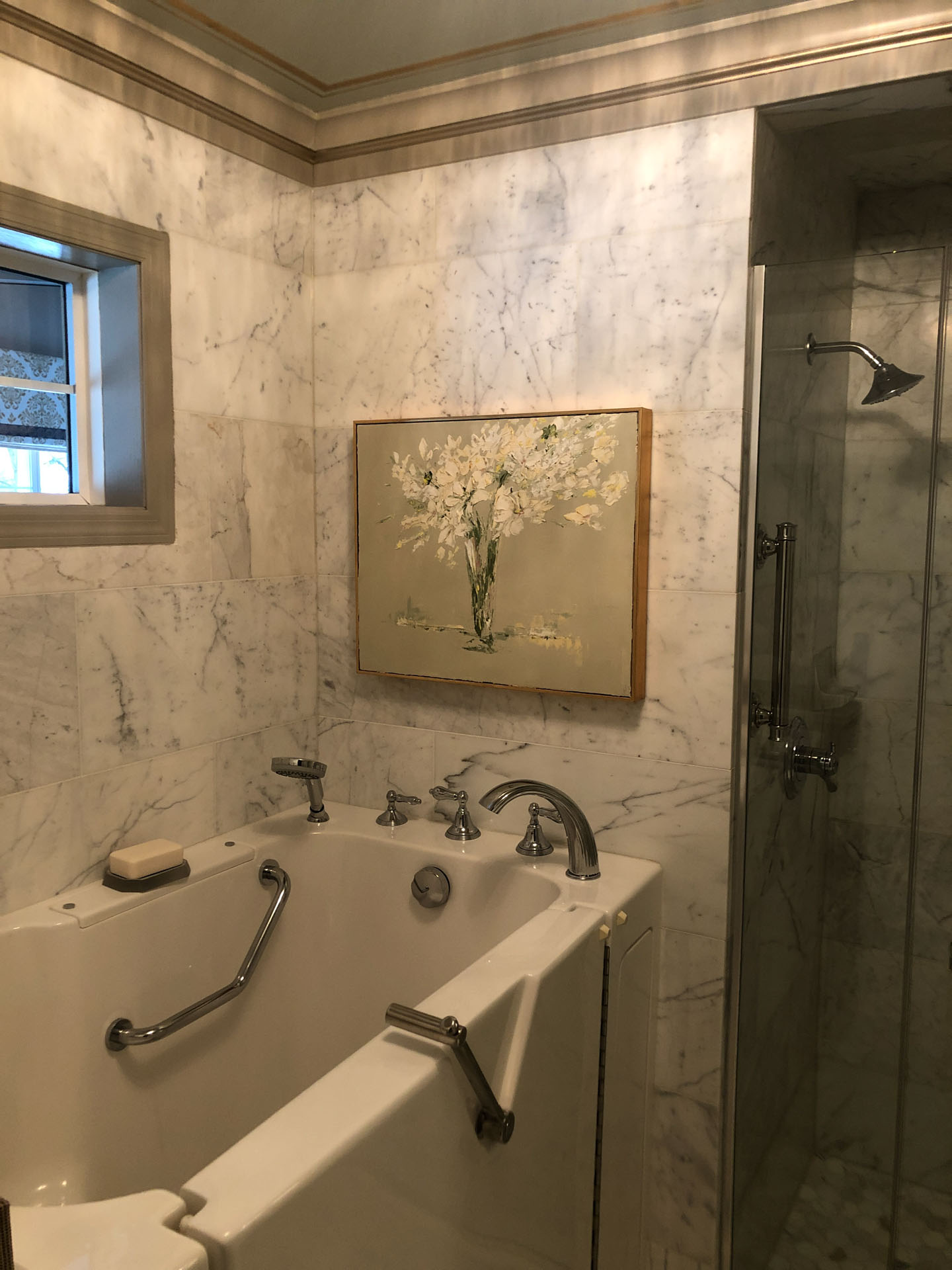 Finished primary bathroom with frameless glass walk-in shower, marble-look porcelain, bench, and mosaic accent