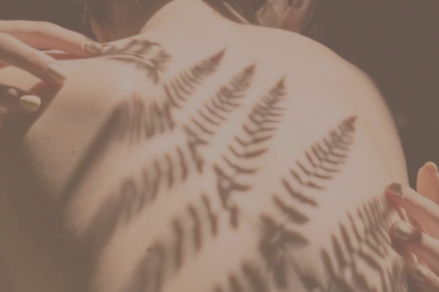 Sunlight and fern shadows on a woman’s back symbolizing emotional healing and feminine embodiment