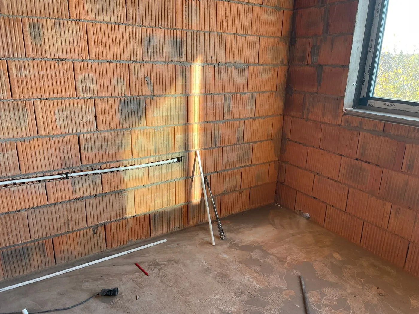 Bruzda pod trasę instalacji klimatyzacji wykuta w ścianie z pustaków, obok długie wiertło i przewody