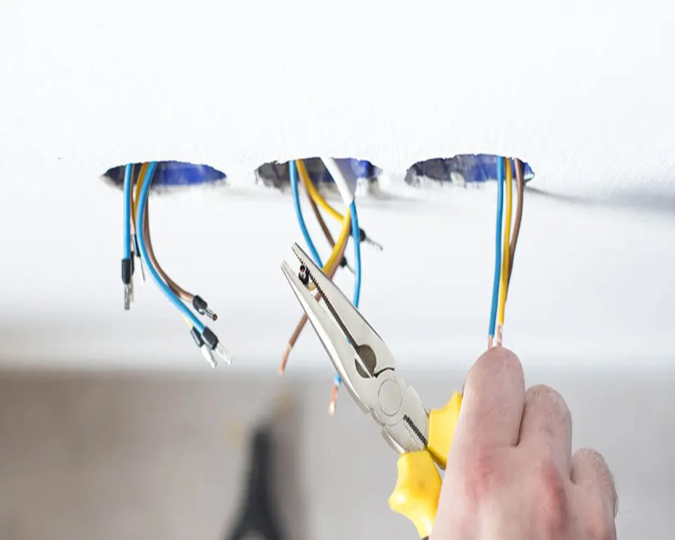 Electrician repairing ceiling electrical wiring with pliers during a residential electrical repair in southern NH