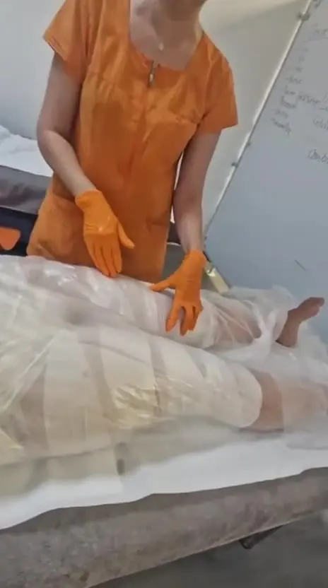 Împachetare corporală cu bandaje, aplicată pe picioarele și abdomenul unei cliente întinse pe pat