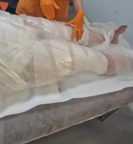 Clientă cu picioarele și corpul &icirc;nvelite &icirc;n folie, &icirc;n timpul unei &icirc;mpachetări corporale &icirc;n salonul din Timișoara