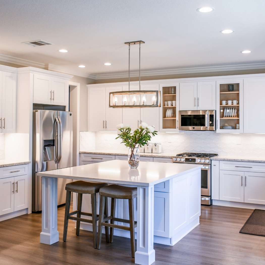 Brand new kitchen with white cabinets set against a white tile backsplash - fitted with a kitchen island and integrated kitchen appliances