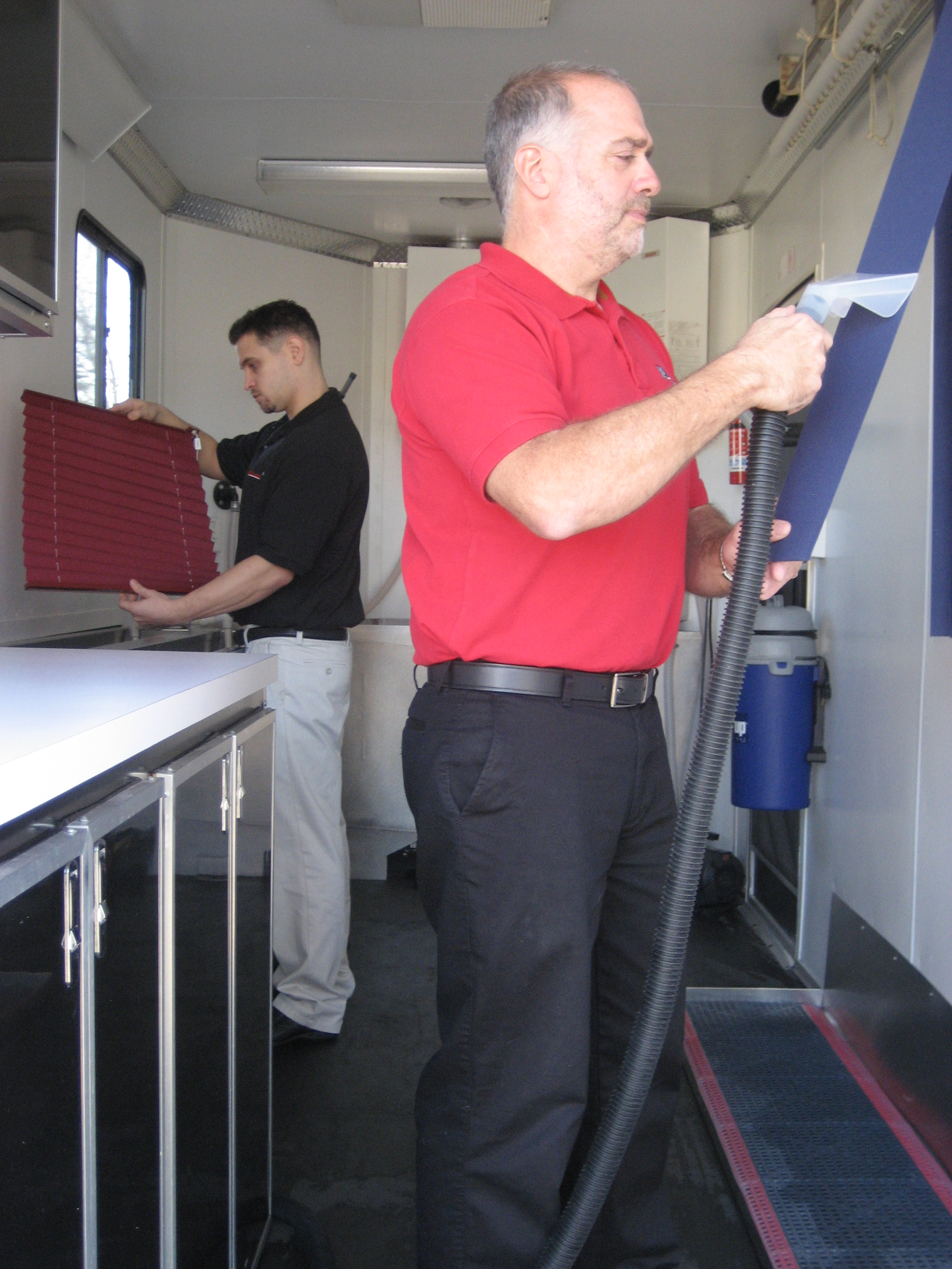 Two operators cleaning blinds inside a mobile trailer