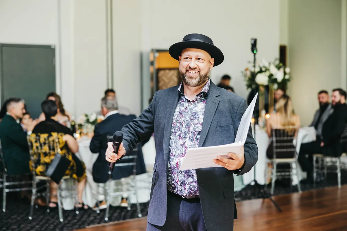 Joe smiling and greeting guests with a microphone at a wedding reception