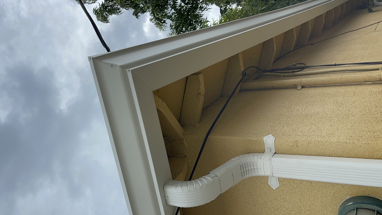 White gutter miter corner and downspout on yellow stucco eave