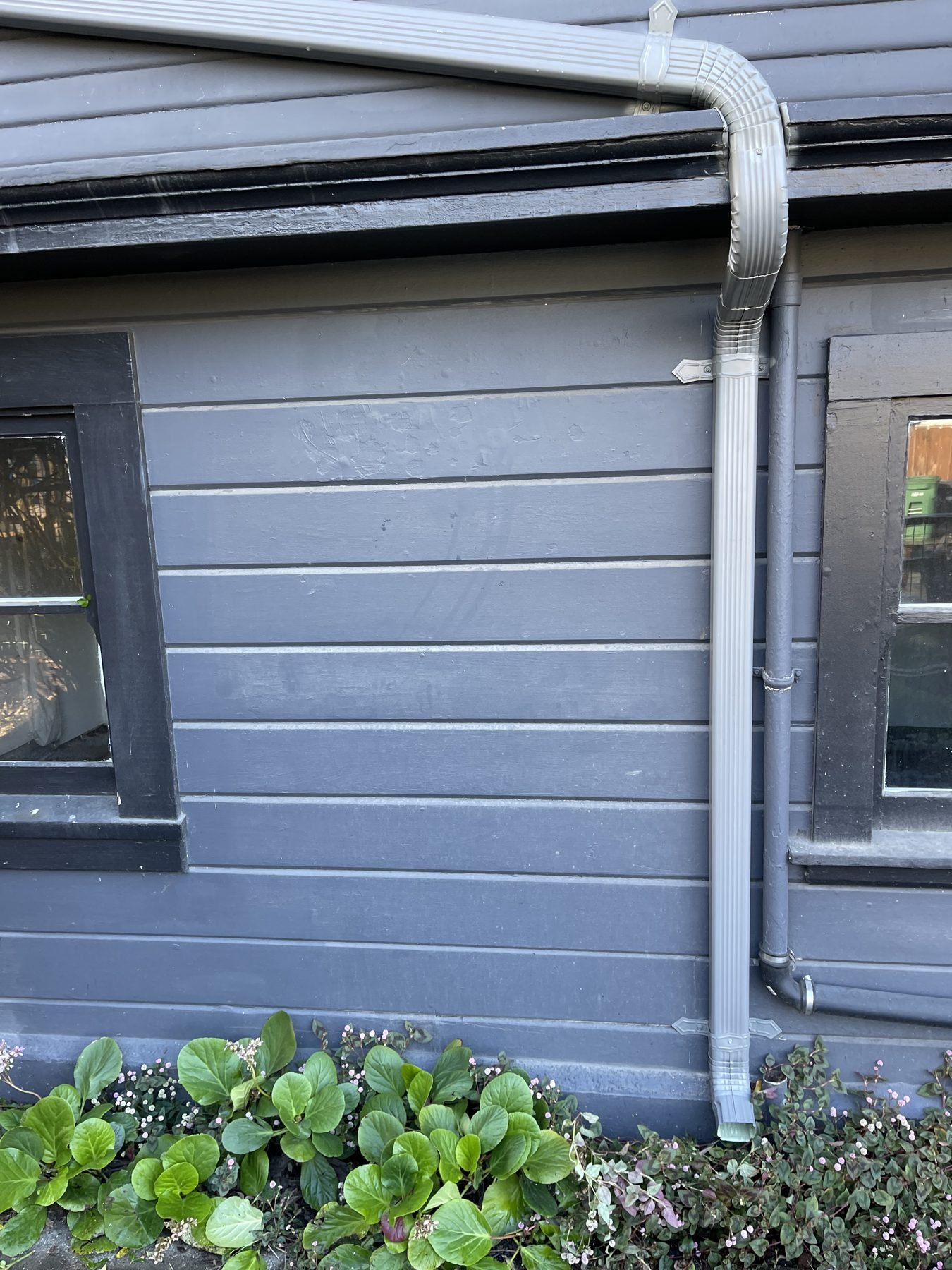 Light-gray downspout directing water away from a Modesto-area home with blue-gray siding