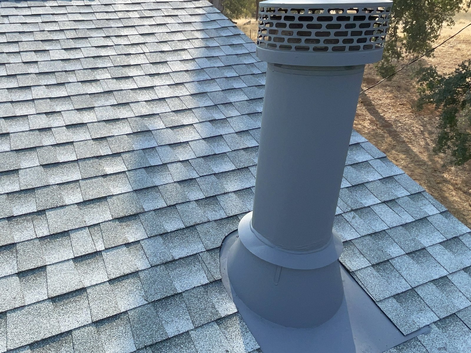 Gray roof vent pipe with conical metal flashing integrated into architectural shingles