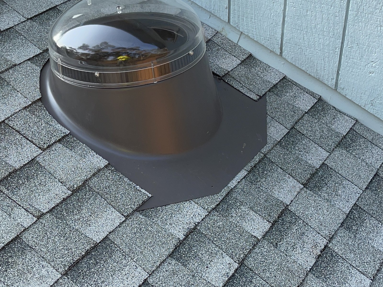 Finished sun-tunnel flashing with a metal base apron woven into gray architectural shingles beside a wall