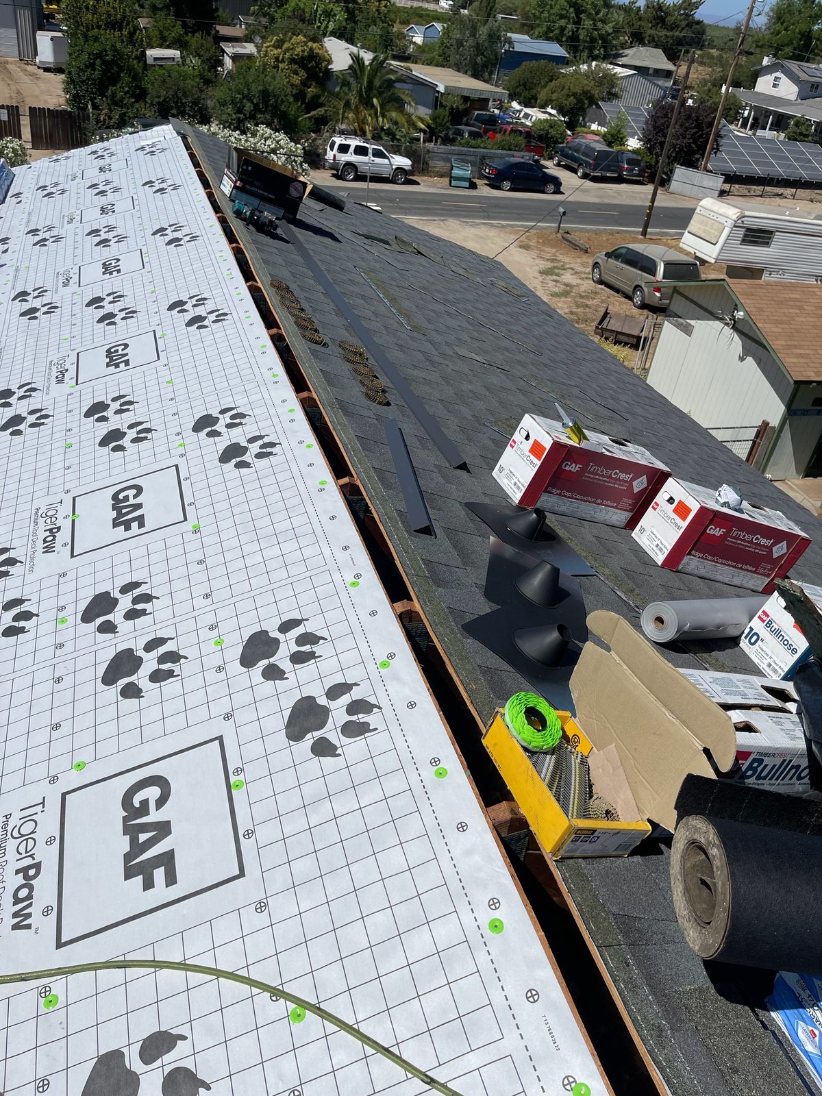 Ridge view during a Modesto roof replacement showing GAF Tiger Paw underlayment meeting new charcoal shingles with TimberCrest ridge-cap boxes and pipe boots staged