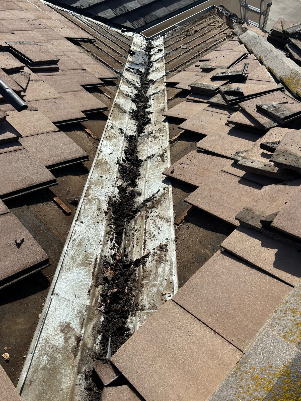 Metal tile roof valley on a Ripon home clogged with packed organic debris between tan concrete tiles