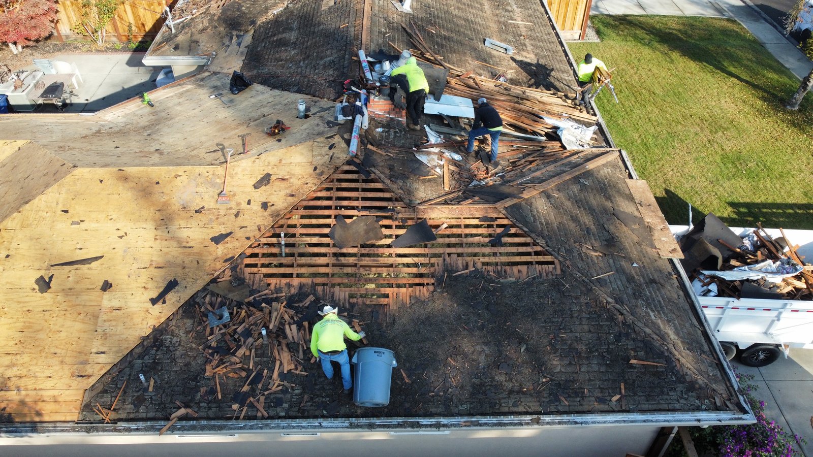 Drone view of a Turlock roof replacement with Legend Roofing crew, exposed skip sheathing, new plywood deck on one wing, and underlayment rolls staged at the ridge