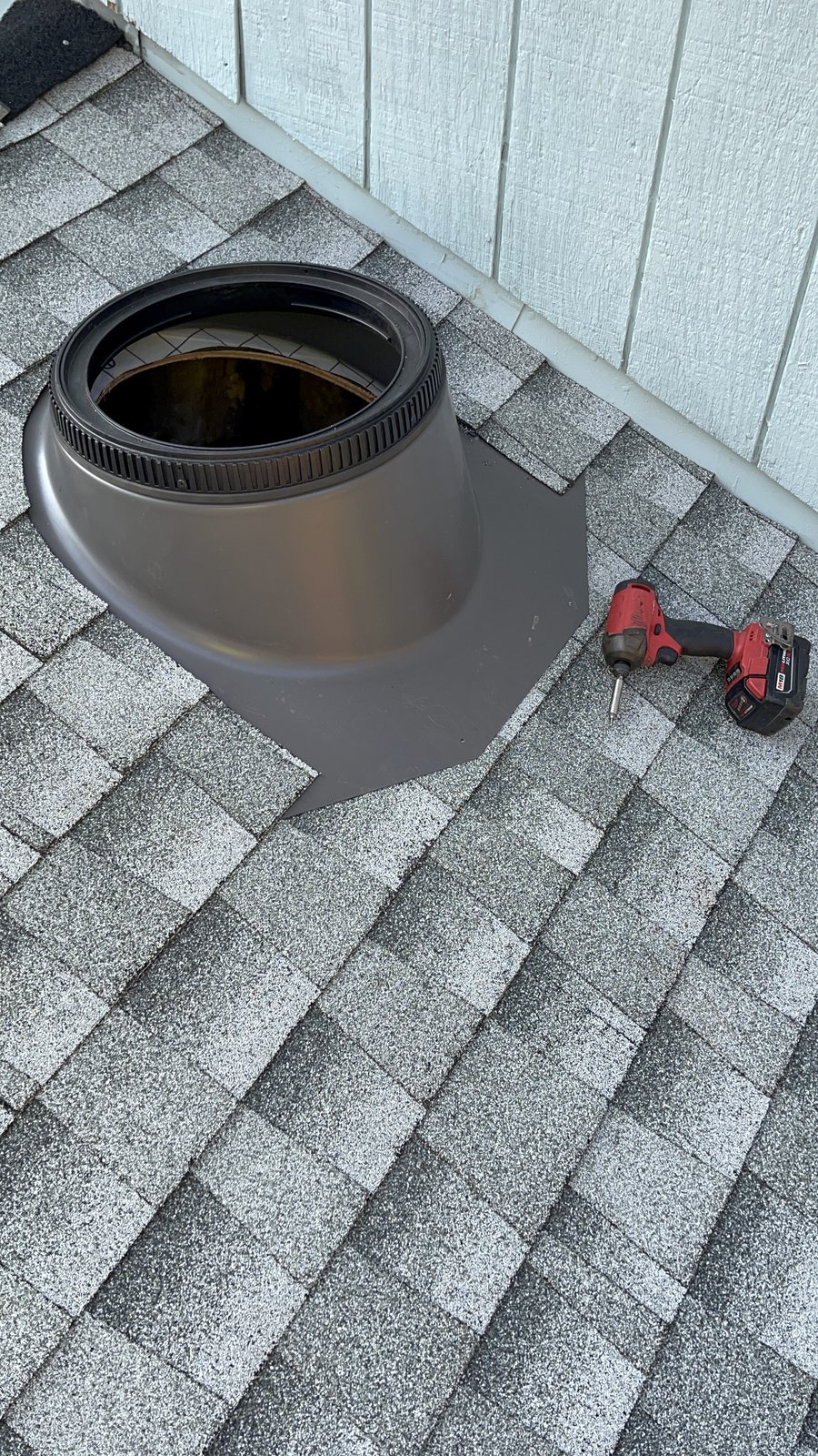 Dark metal sun tunnel flashing base integrated into gray architectural shingles on a Central Valley roof, Milwaukee impact driver resting nearby during installation