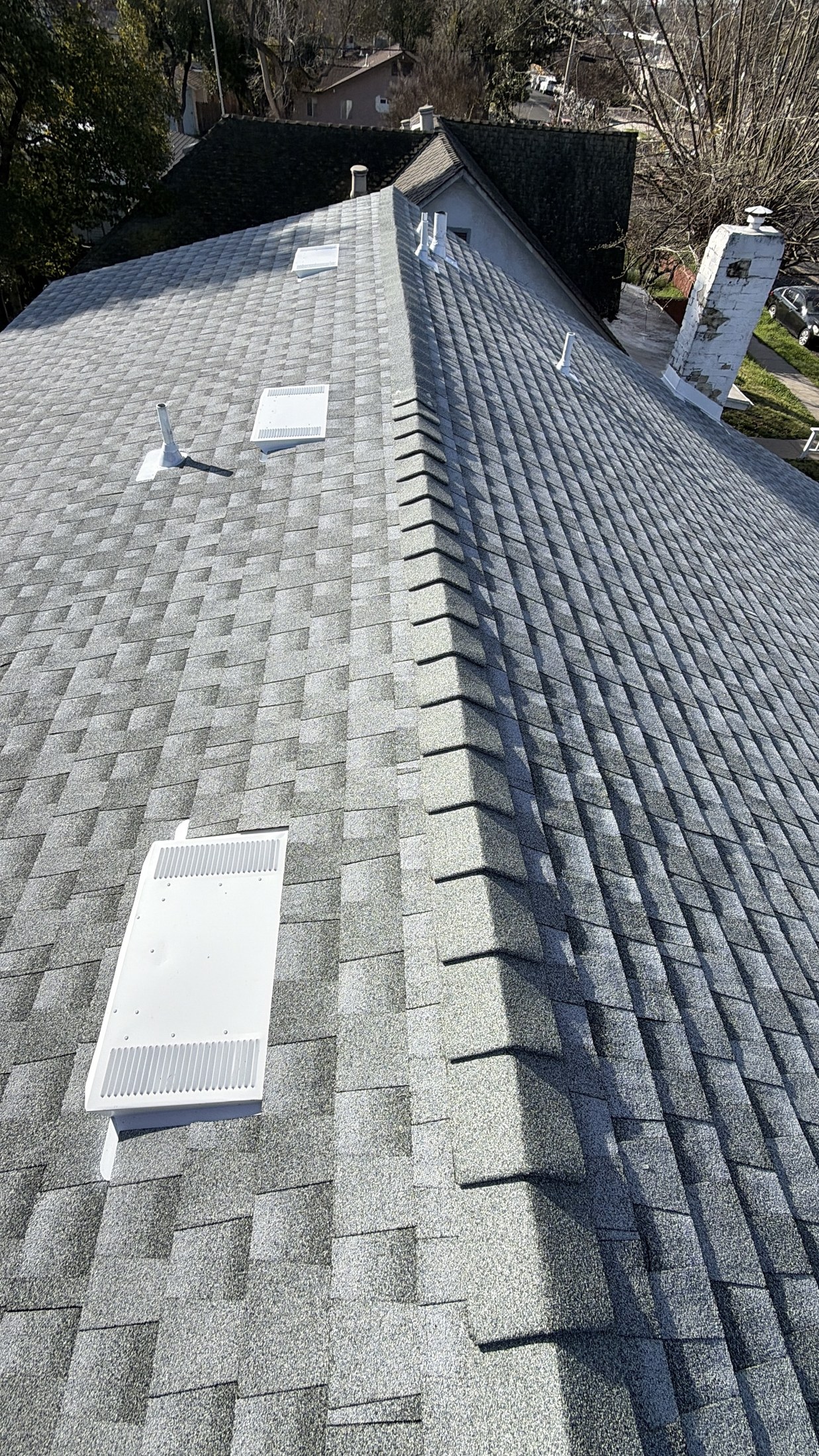 Gray architectural asphalt shingles on a residential roof ridge with off-ridge box vents