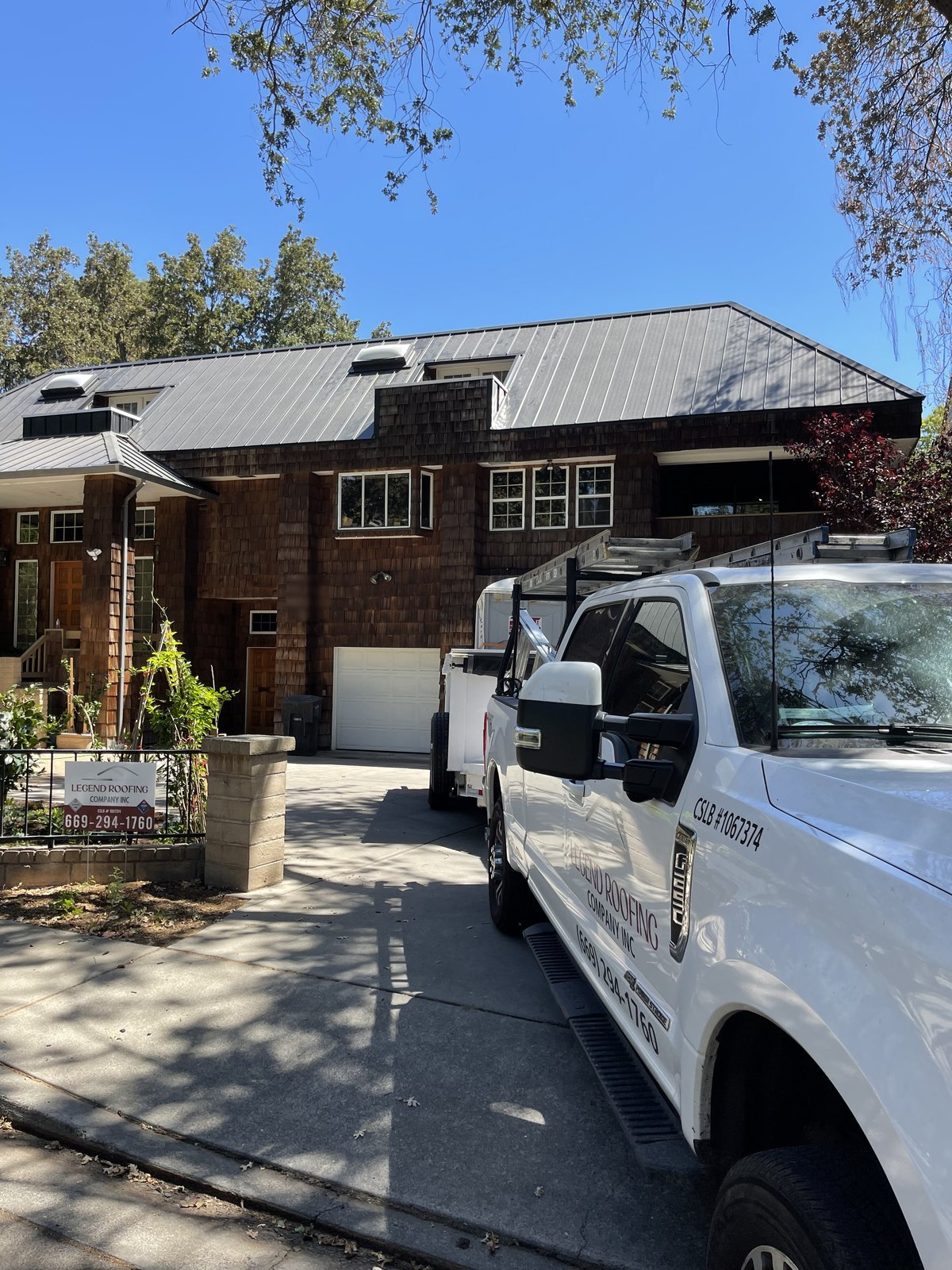 Finished charcoal standing seam metal roof on a multi-story home with Legend Roofing Company Inc truck showing (669) 294-1760 and CSLB #1067374