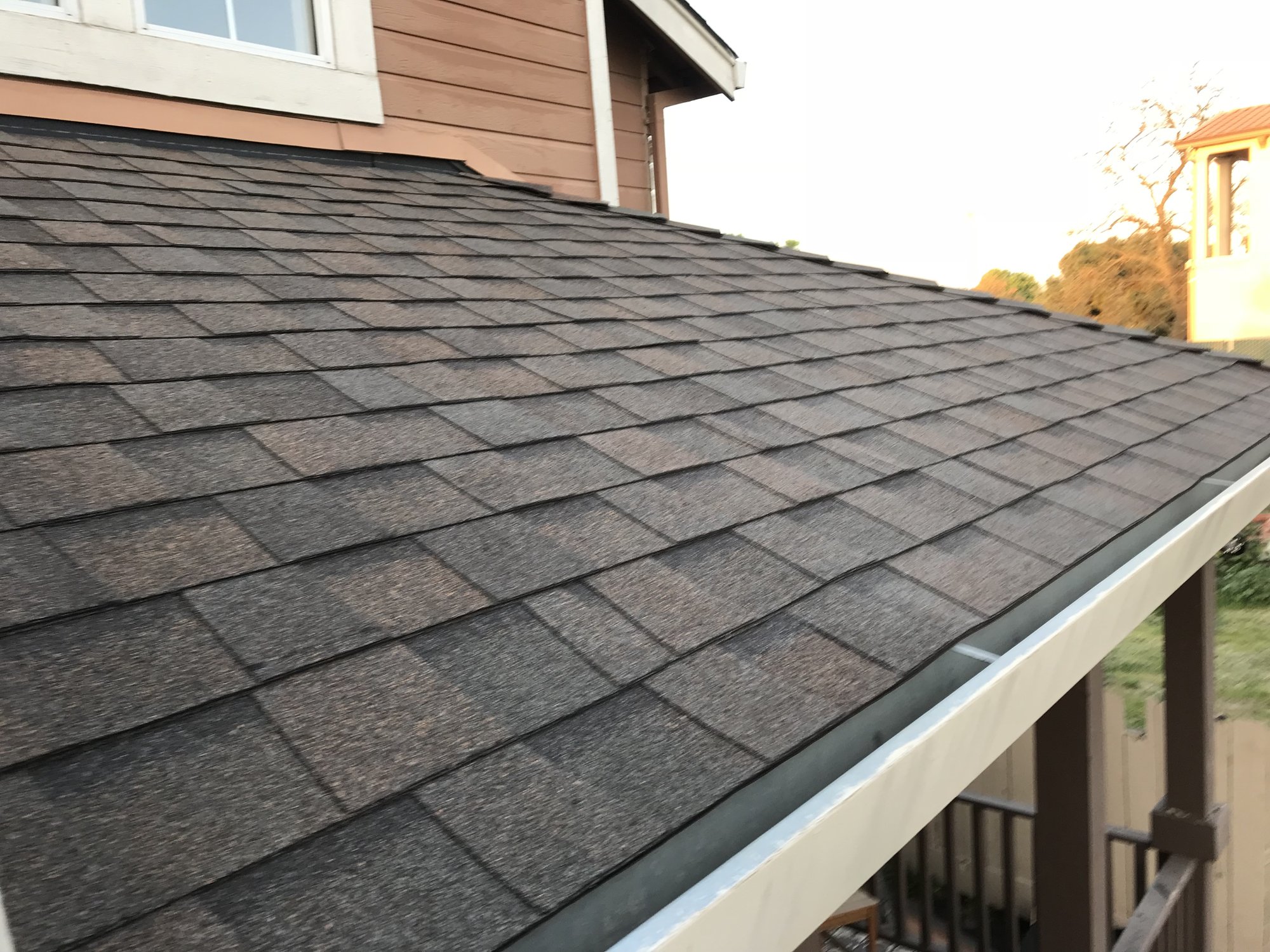 Architectural asphalt shingles meeting a gray metal drip edge and white seamless gutter along a residential roof eave