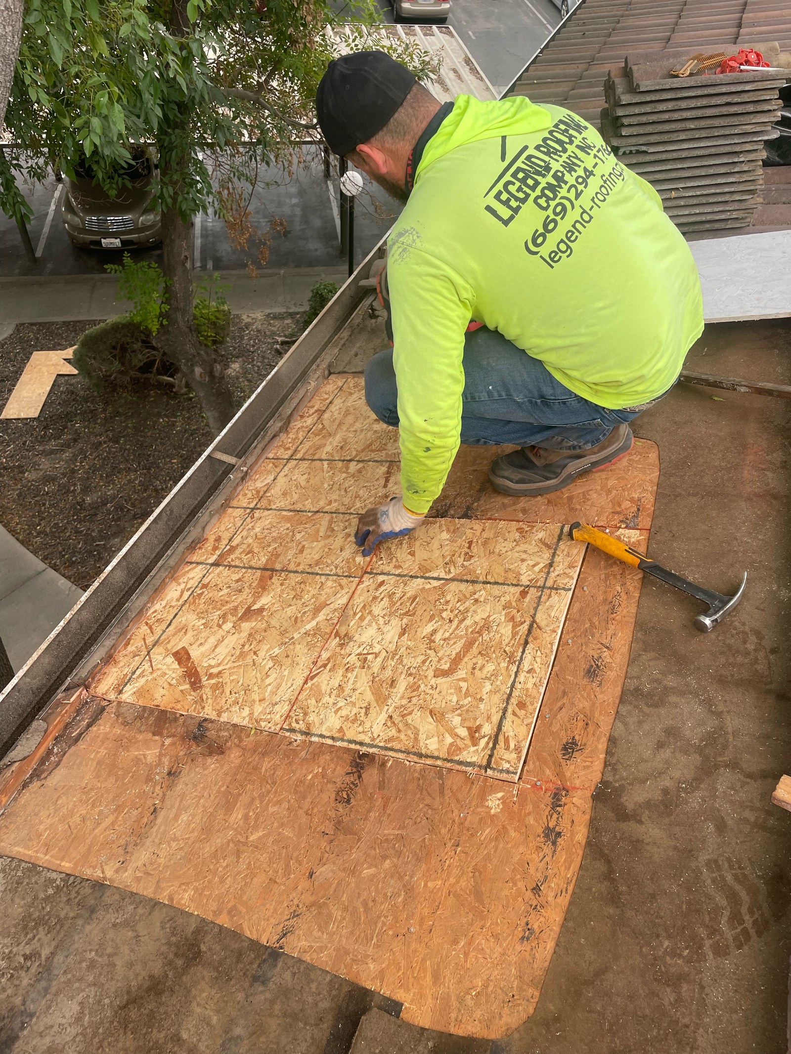Legend Roofing Company Inc crew member fitting a new OSB decking patch into an opened tile roof