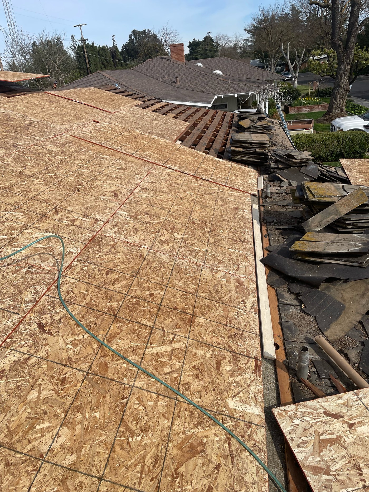 Modesto residential roof mid-replacement with new OSB sheathing on the main slope, exposed rafters, and piles of tear-off debris along the eave