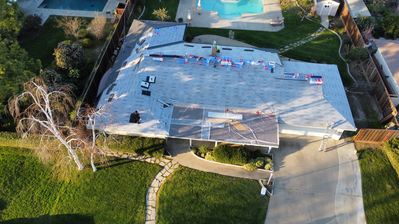 Overhead view of the same Modesto roof fully dried in with synthetic underlayment and GAF shingle bundles staged along the ridge