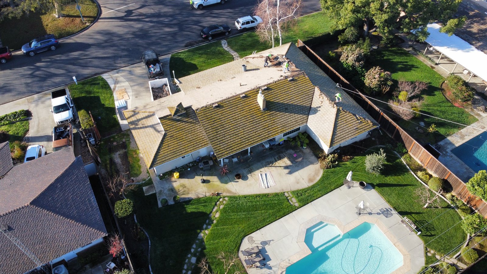 Drone view of a Modesto home mid tile tear-off with moss-darkened concrete tile and Legend Roofing Company Inc crew at the ridge