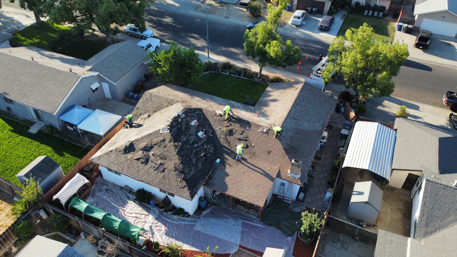 Drone view of a Riverbank home during roof tear-off with Legend Roofing Company Inc crew removing old shingles and tarps over the yard