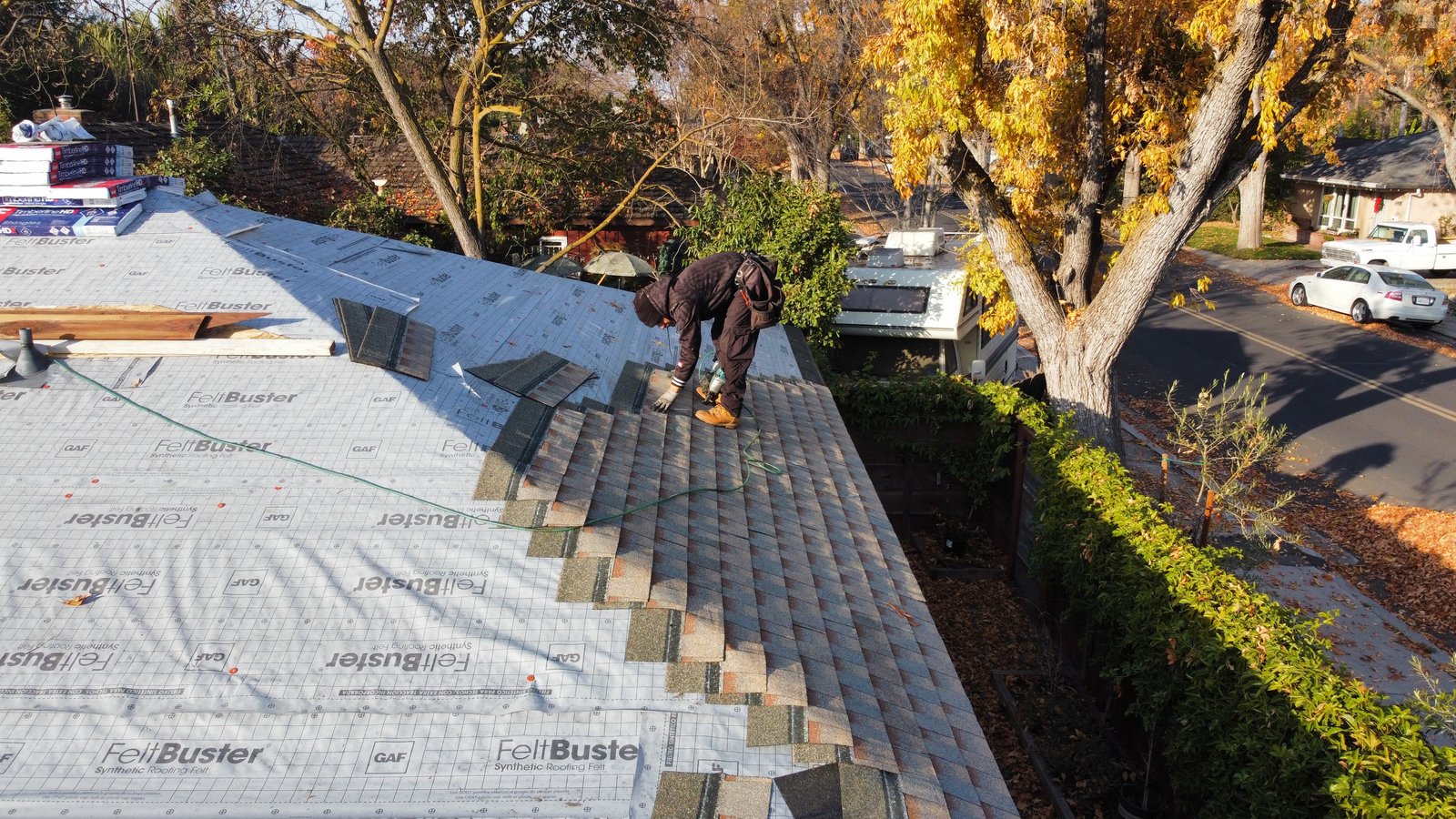 Legend Roofing Company Inc crew member fastening GAF Timberline HDZ shingles in Copper Canyon over GAF FeltBuster synthetic underlayment on a Modesto roof, with fall leaves on the street below