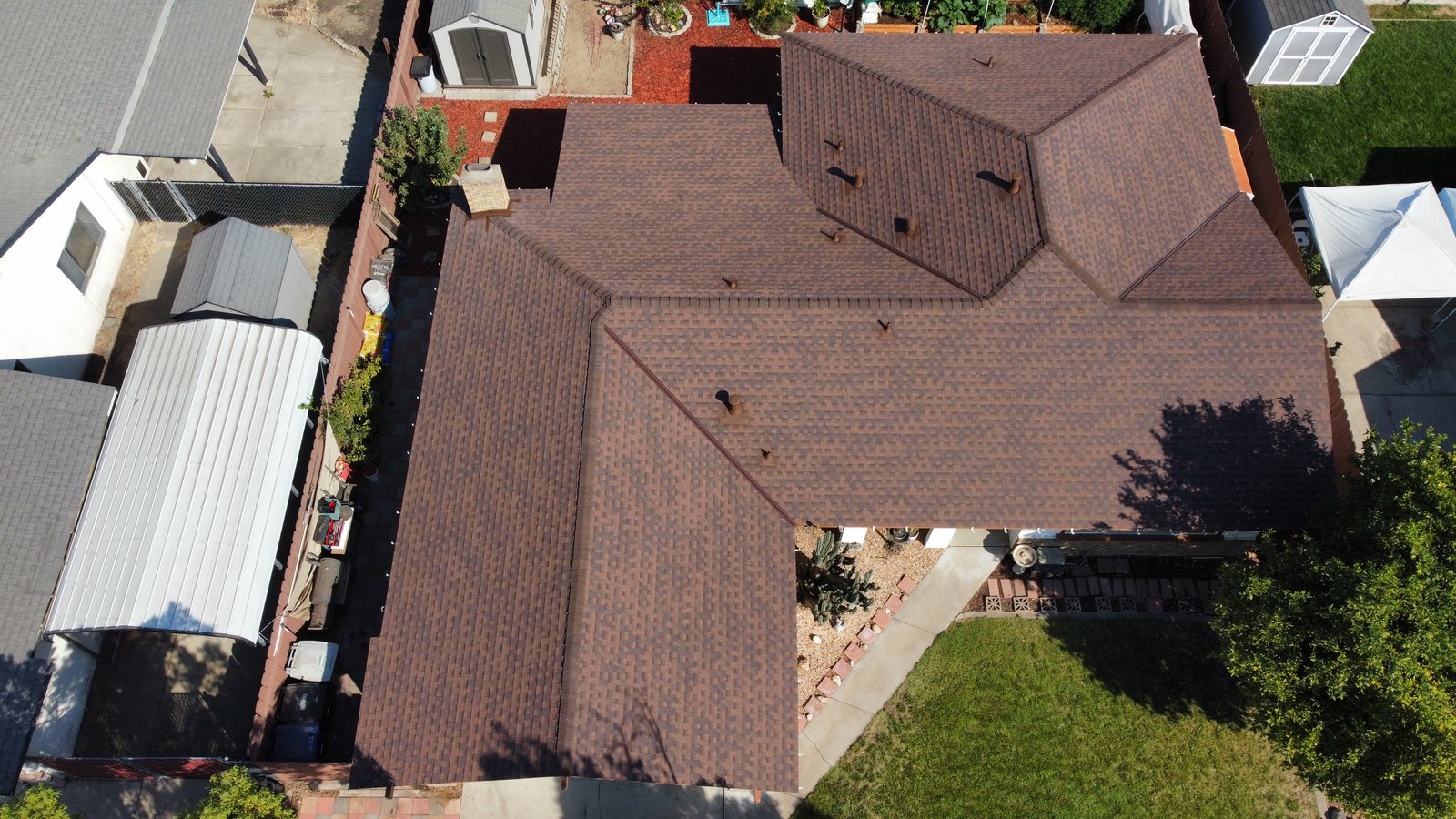 Wider drone view of the same Riverbank home with a complete GAF Timberline Hickory shingle roof, color-matched vents and the surrounding yard