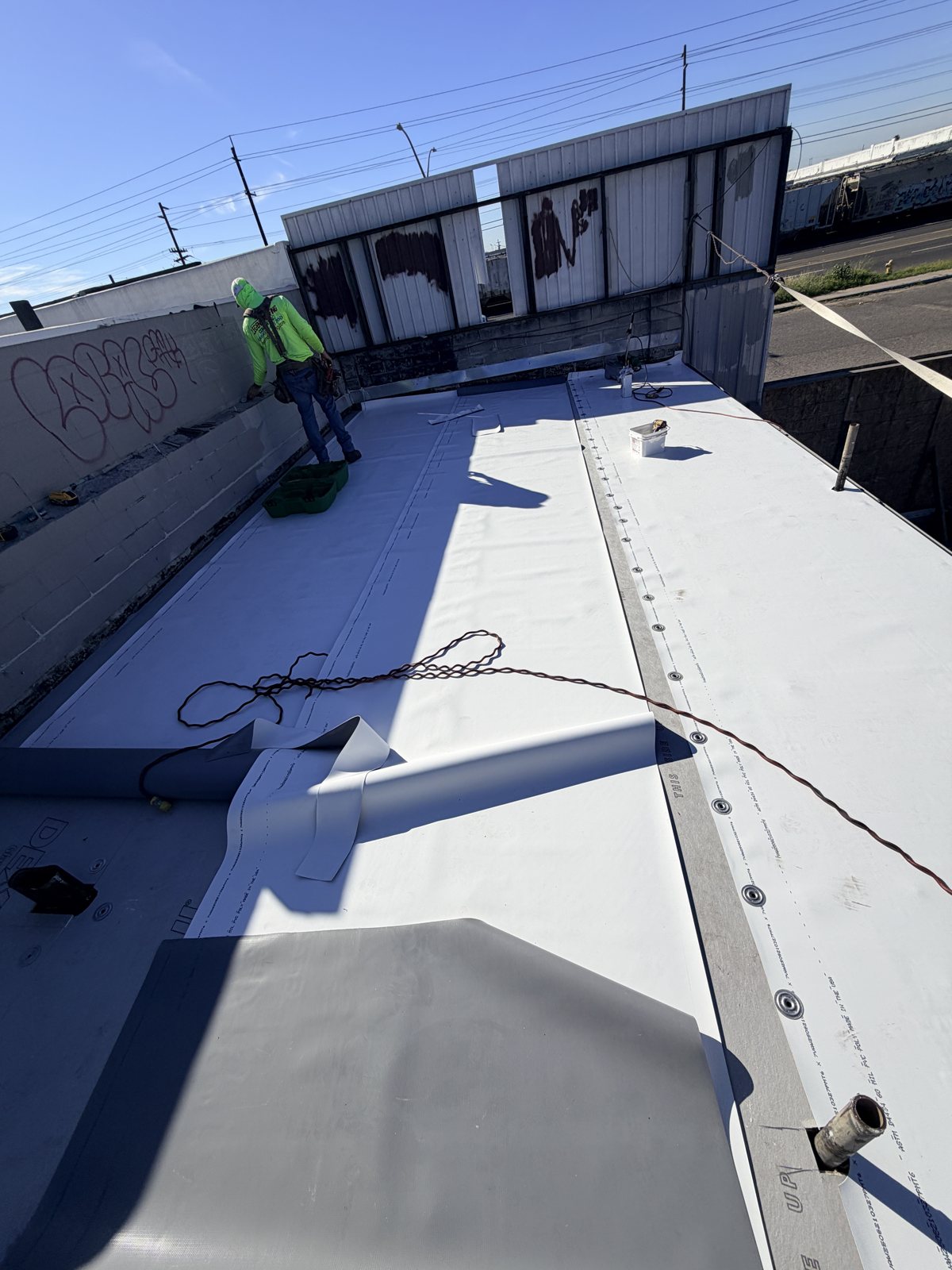 Mechanically fastened TPO roof with a row of round fastener plates along the edge of one sheet, the welded lap line of the next sheet, and a Legend Roofing crew member near the parapet wall