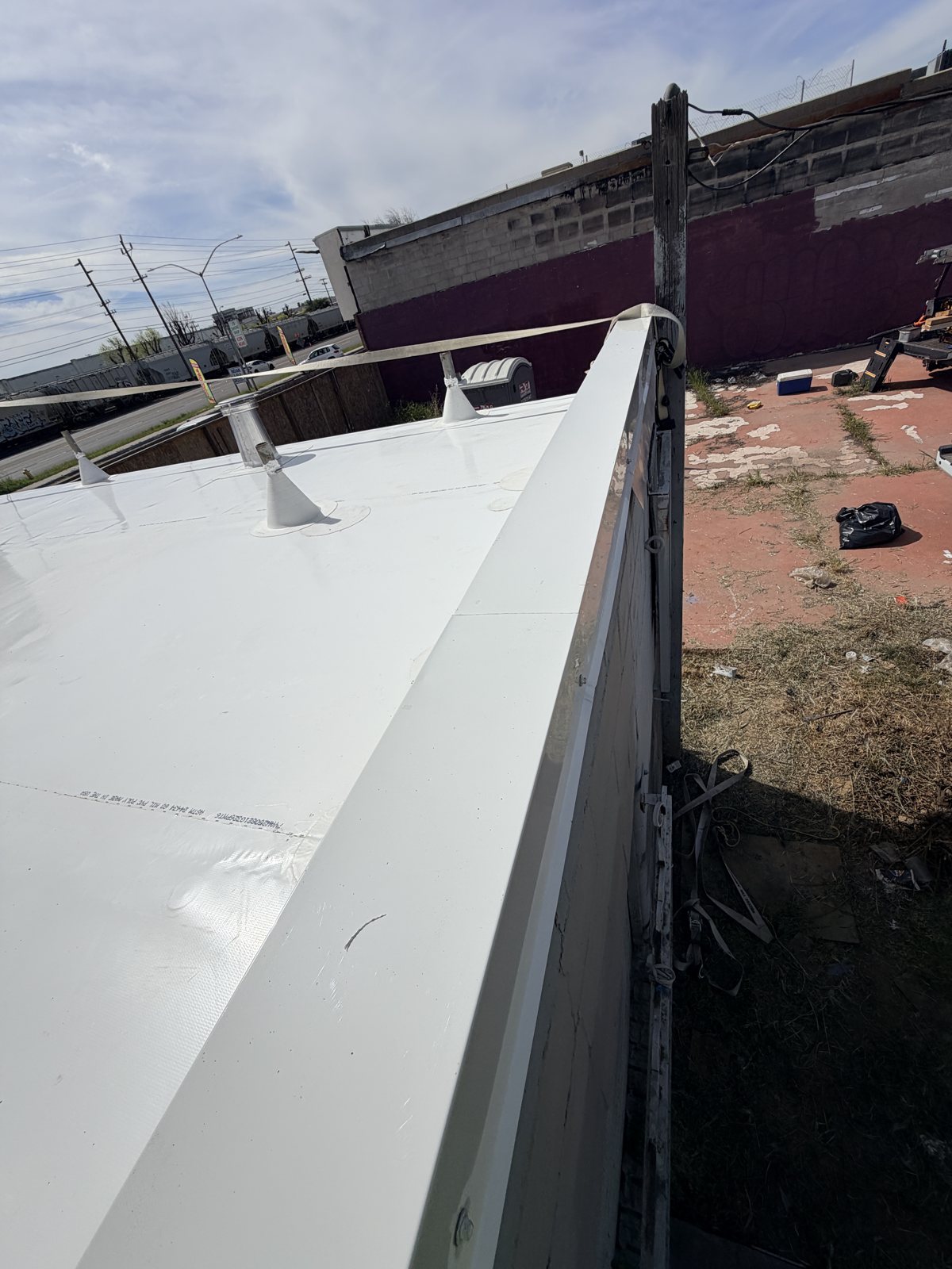 Edge of a white TPO roof where the membrane wraps up and over the wall top, with cone-shaped TPO pipe boots flashed around two pipes in the field
