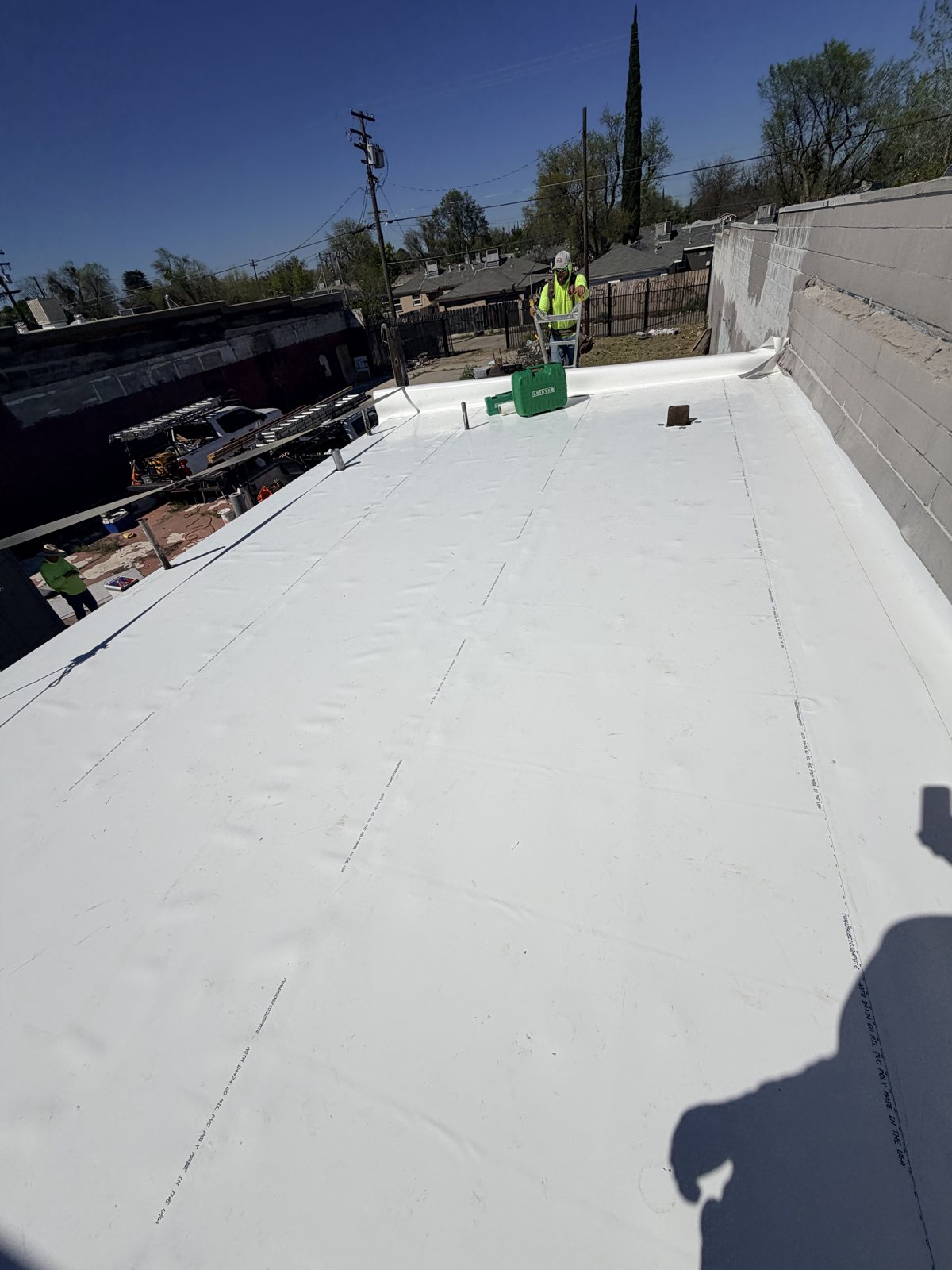 Legend Roofing crew on a finished white TPO low-slope roof, with a hot-air seam welder case on the membrane and a block parapet wall along one side