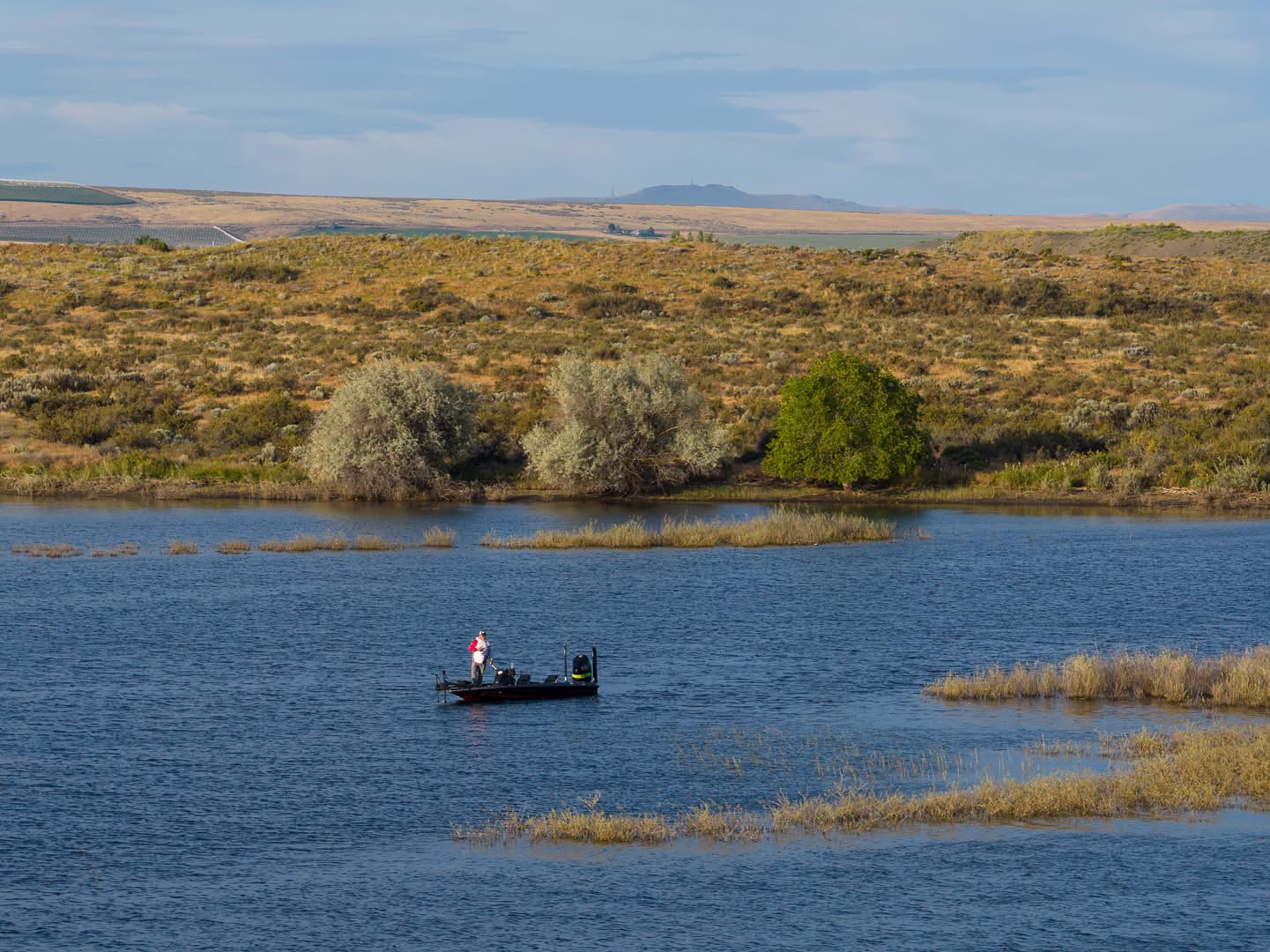Sam fishing alone on a blue lake below sage hills