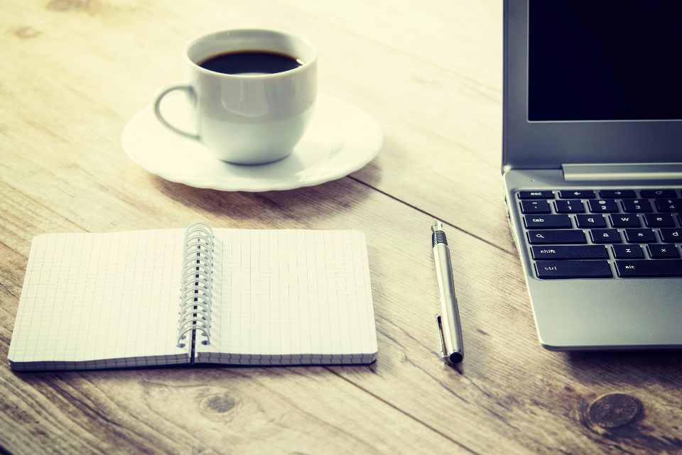 Coffee, notebook, and laptop on a wooden desk