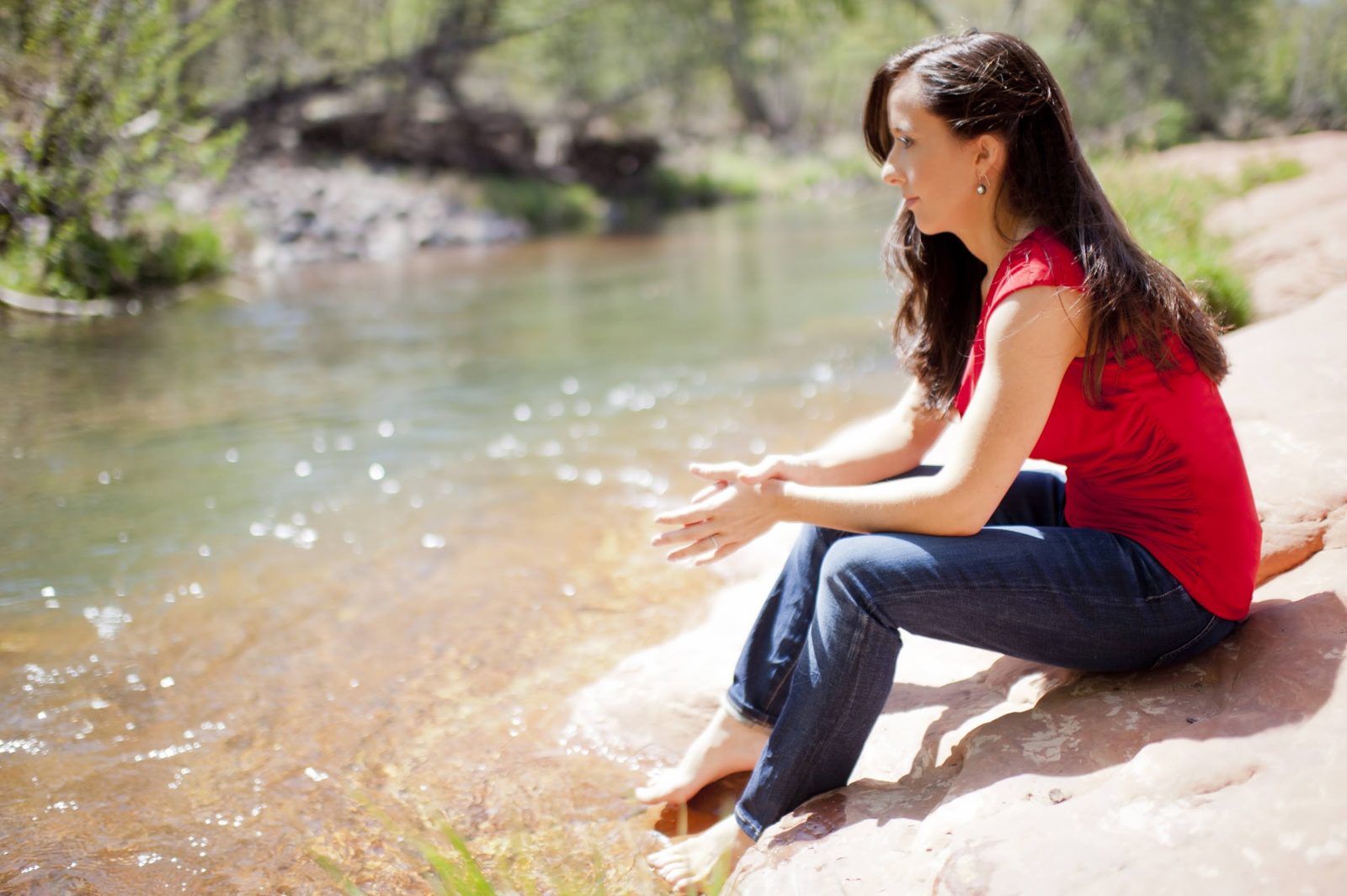 Mindie sitting on a rock by a creek in a red top