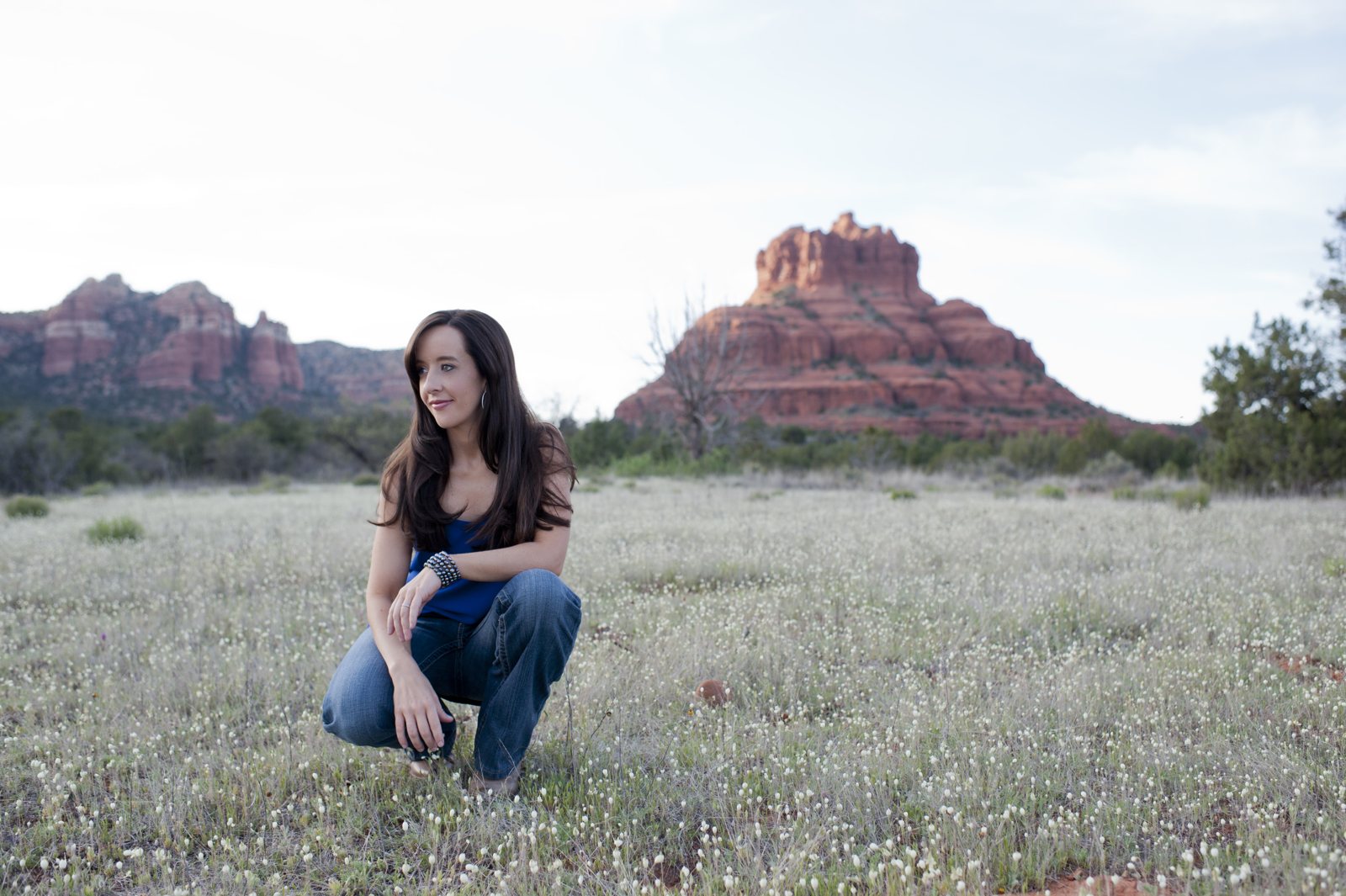 Mindie Kniss crouching in a wildflower field with Bell Rock behind her