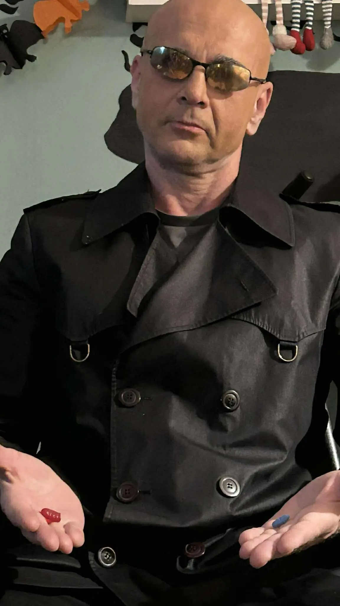 Janos dressed as Morpheus for Halloween holding red and blue capsules with sunglasses indoors