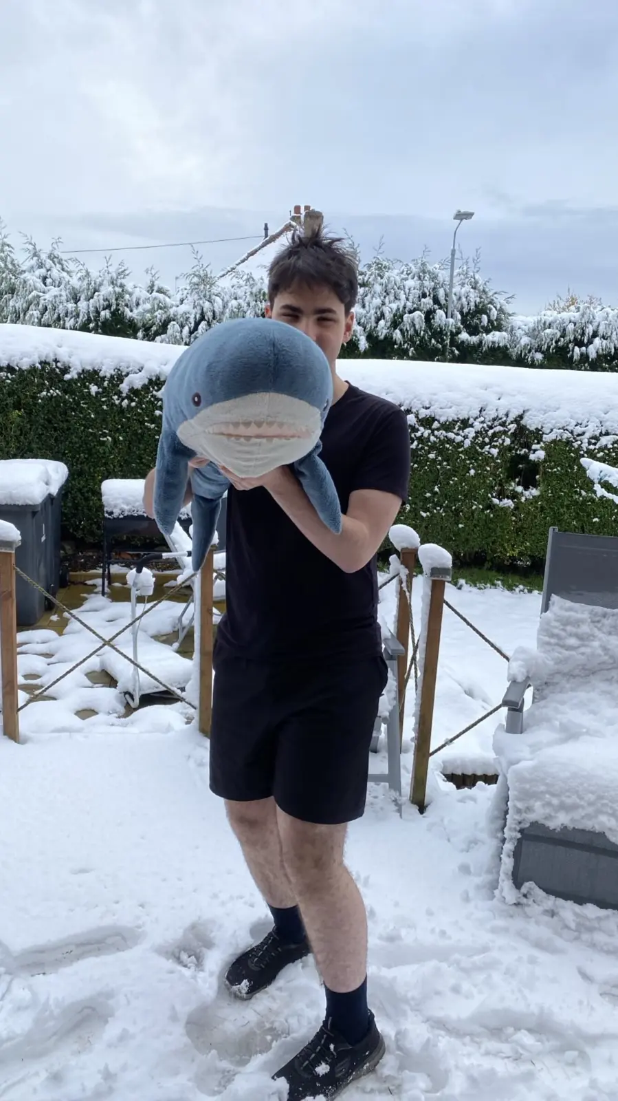Kristof standing in snow wearing shorts and holding a large IKEA plush shark