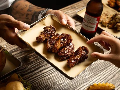 Hands sharing a tray of Chinese bourbon wings with beer and loaded fries