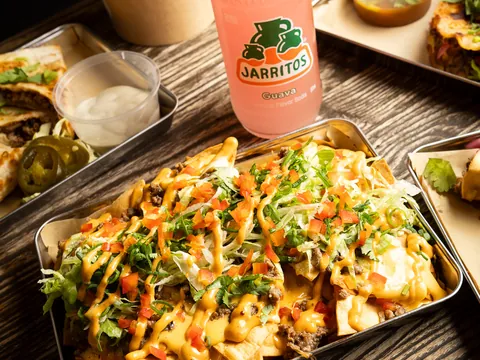 A tray of loaded nachos beside a bottle of Jarritos
