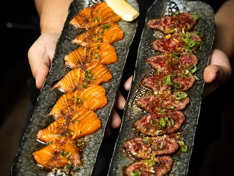 Two long platters of seared salmon and beef held out to the camera