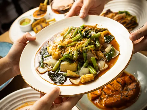 Hands passing a plate of pad cha tofu across a shared table