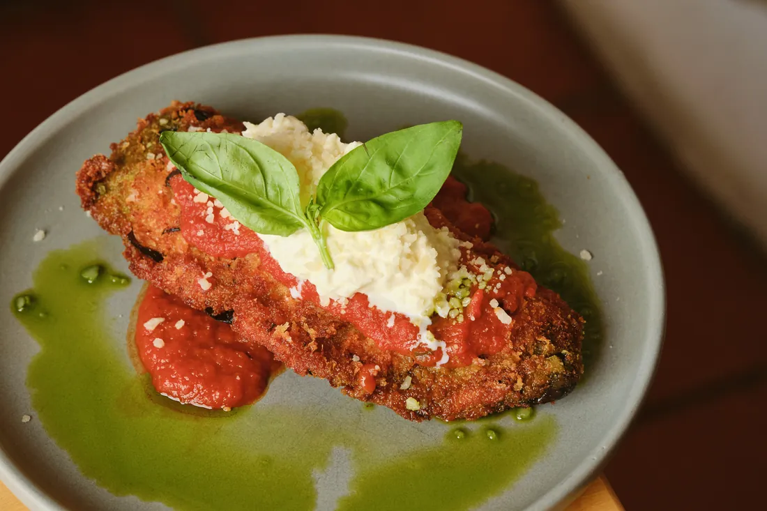 A crumbed cutlet under tomato sauce, grated cheese and basil on green oil