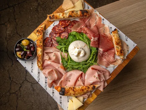 Prosciutto, rocket and a ball of burrata on a pizza crust board, from above