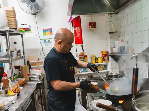 A chef tossing a smoking wok in the At Thai Lindfield kitchen